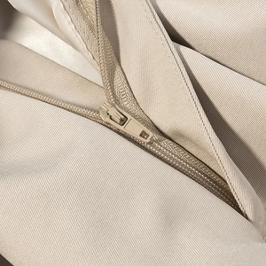 Close-up of a high-quality beige zipper detail on textured twill fabric jacket
