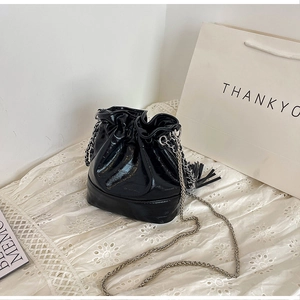 Close-up of a glossy black bucket bag with chain strap and tassels on white lace fabric