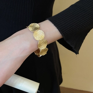 Detail of gold-tone hammer-textured elastic bracelet worn on wrist over black sleeve