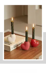 Detail of ceramic heart candle holders with textured green taper candles on a wooden table