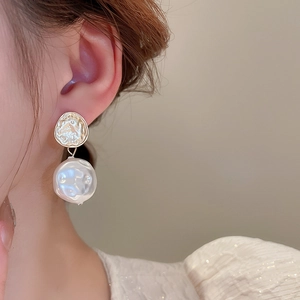 Dettaglio orecchino dorato con texture irregolare e perla barocca indossato su modella