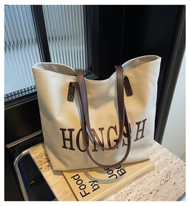 Detail of large canvas tote bag with HONGSH letter print and brown leather handles