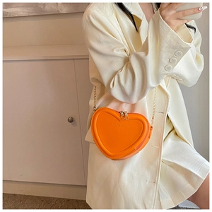 Detail der leuchtend orangefarbenen Herztasche mit Metallkette und Logo-Textur