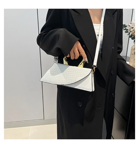 White crocodile pattern handbag with geometric design and gold handle held by model