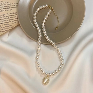 Elegant pearl necklace with oval gemstone pendant on a vintage beige silk background