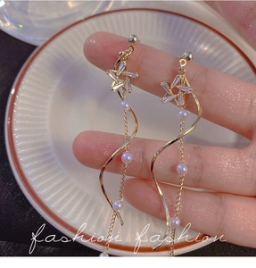Detail of star-shaped earrings with long pearls and spiral fringe in golden finish