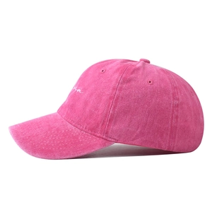 Detail of white cursive embroidery on a vintage washed pink baseball cap with fabric texture