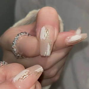 Macro shot of long coffin fake nails with nude pink base, gold leaf and white brush strokes