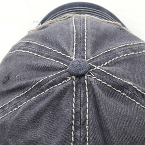 Macro detail of washed cotton baseball cap showing contrast stitching and crown button