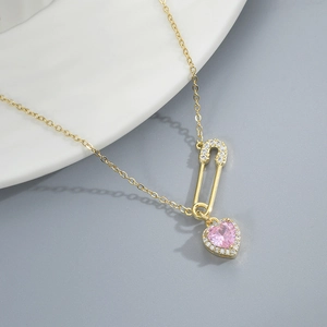 Detailed macro view of gold safety pin pendant with pink heart gemstone and pavé stones