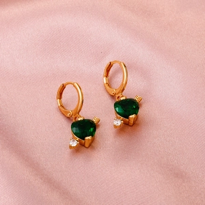 Detail of heart-shaped green zircon earrings with golden metal finish on pink silk