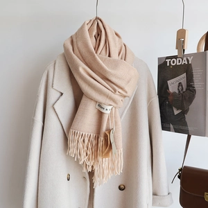 Detail of beige cashmere-feel scarf featuring tassel edges and a sewn-on textile label