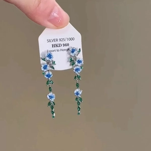 Détail de boucles d'oreilles fleur en argent 925 avec émail bleu et gemmes vertes
