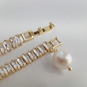 Macro d'un bracelet doré avec zircons rectangulaires, perle blanche et fermoir à rabat