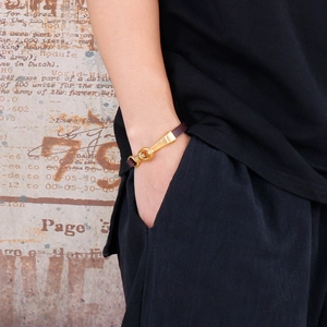 Detail of dark brown leather braided bracelet with polished gold U-shaped metal clasp