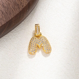 Close-up of golden letter M pendant with micro-paved cubic zirconia on textured background