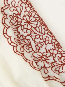 Detailed macro view of reddish-brown floral embroidery on white cotton linen fabric