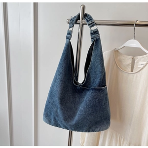 Blue denim tote bag detail showing shoulder strap hanging on a minimalist metal rack