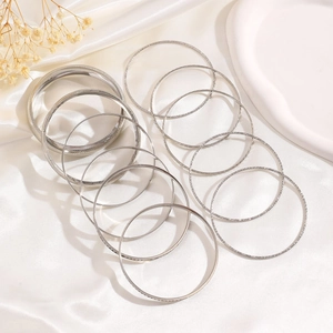 Macro detail of 14-piece silver bangles set with polished and textured finishes on silk