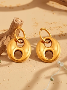 Detailed view of gold geometric hollow earrings with polished surface on a sandy background