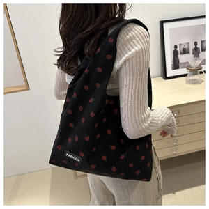 Black corduroy tote bag with red strawberry print shown on model in home setting
