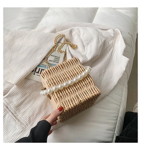 Detail of woven straw bag with faux pearl handle and gold chain on corduroy cloth