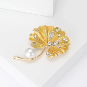 Close-up of golden leaf brooch featuring clear rhinestones and a white faux pearl detail