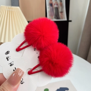 Detail of red plush fur ball hair clips on metal base attached to white card packaging