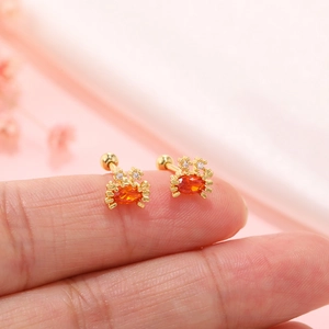 Detailed close-up of tiny crab-shaped gold earrings with orange gemstones on a fingertip
