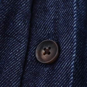 Makro-Detail von braunen Knöpfen auf dunkelblauem Jeanskleid mit feiner Stoffstruktur