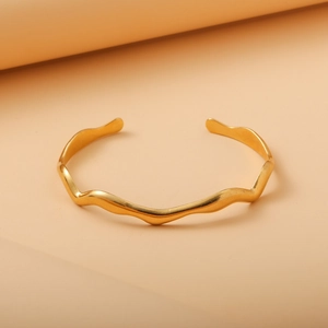 Close-up of golden wavy cuff bracelet with irregular curved lines and polished finish