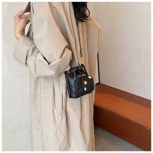 Chic black drawstring bucket bag with gold chain strap shown on model over a beige coat