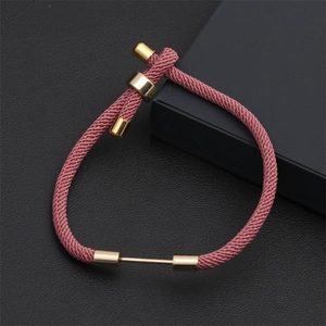 Detail of adjustable pink woven Milan rope bracelet with gold metal hardware on black leather