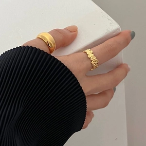 Close-up of stacked gold irregular wave rings on model against textured background