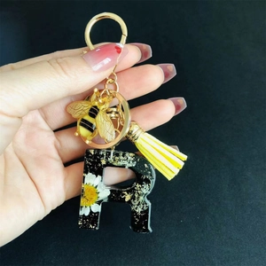 Detail of resin letter R keychain with dried flowers, gold foil, bee charm and yellow tassel