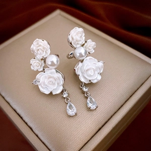 Close-up of white resin rose earrings with pearl accents and teardrop zircon drop