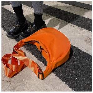 Detailed top view of a bright orange nylon crescent crossbody bag on a street pavement
