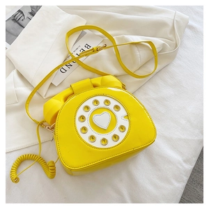 Detail shot of a yellow vintage telephone-shaped crossbody bag with a heart dial