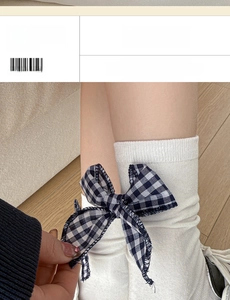 Detail of white ribbed cotton socks featuring a blue plaid bow on a warm wooden floor