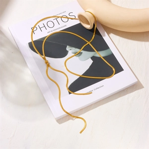 Flat golden snake chain necklace on white fashion magazine with soft shadow detail