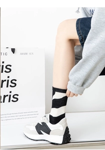 Close-up of black and white striped crew socks with grey sneakers on white background