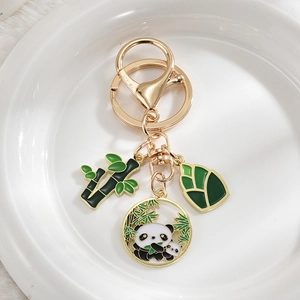 Close-up of panda and bamboo enamel pendants with gold-plated keychain on white plush base