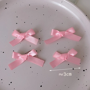 Close-up of four mini 3cm pink satin bow hair clips on a decorative ceramic plate