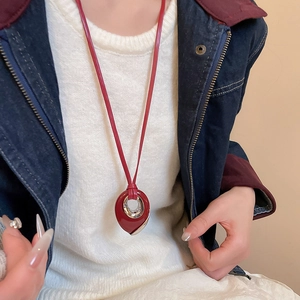 Close-up of red waterdrop pendant necklace with metal ring on model wearing a white sweater