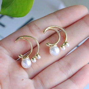 Close-up of gold geometric earrings with elegant white pearls held in hand