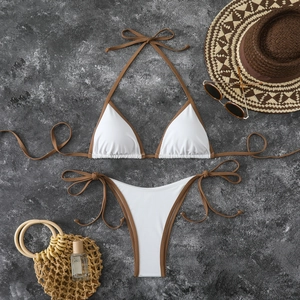 Flat lay of white bikini set with brown straps, beach hat and sunglasses on stone background