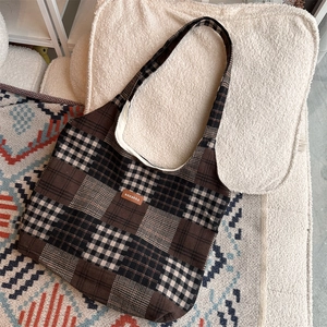 Dettaglio macro della borsa tote patchwork scozzese marrone con etichetta logo in pelle