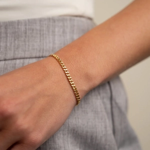 Detailed view of a delicate 14k gold-plated Cuban link chain bracelet on a model's wrist