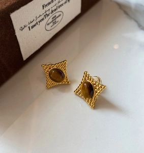 Vue détaillée des boucles d'oreilles œil de tigre avec gravure étoile dorée sur marbre