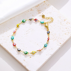 Detail of gold evil eye bracelet with colorful enamel beads on white marble surface